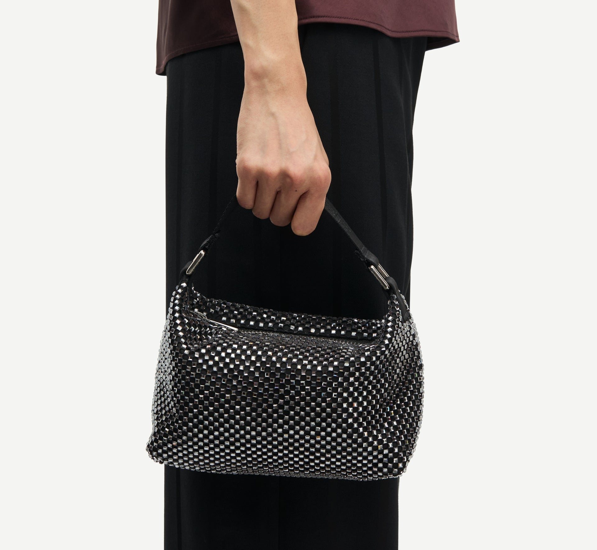 Person holding a black handbag with a textured pattern against a plain background